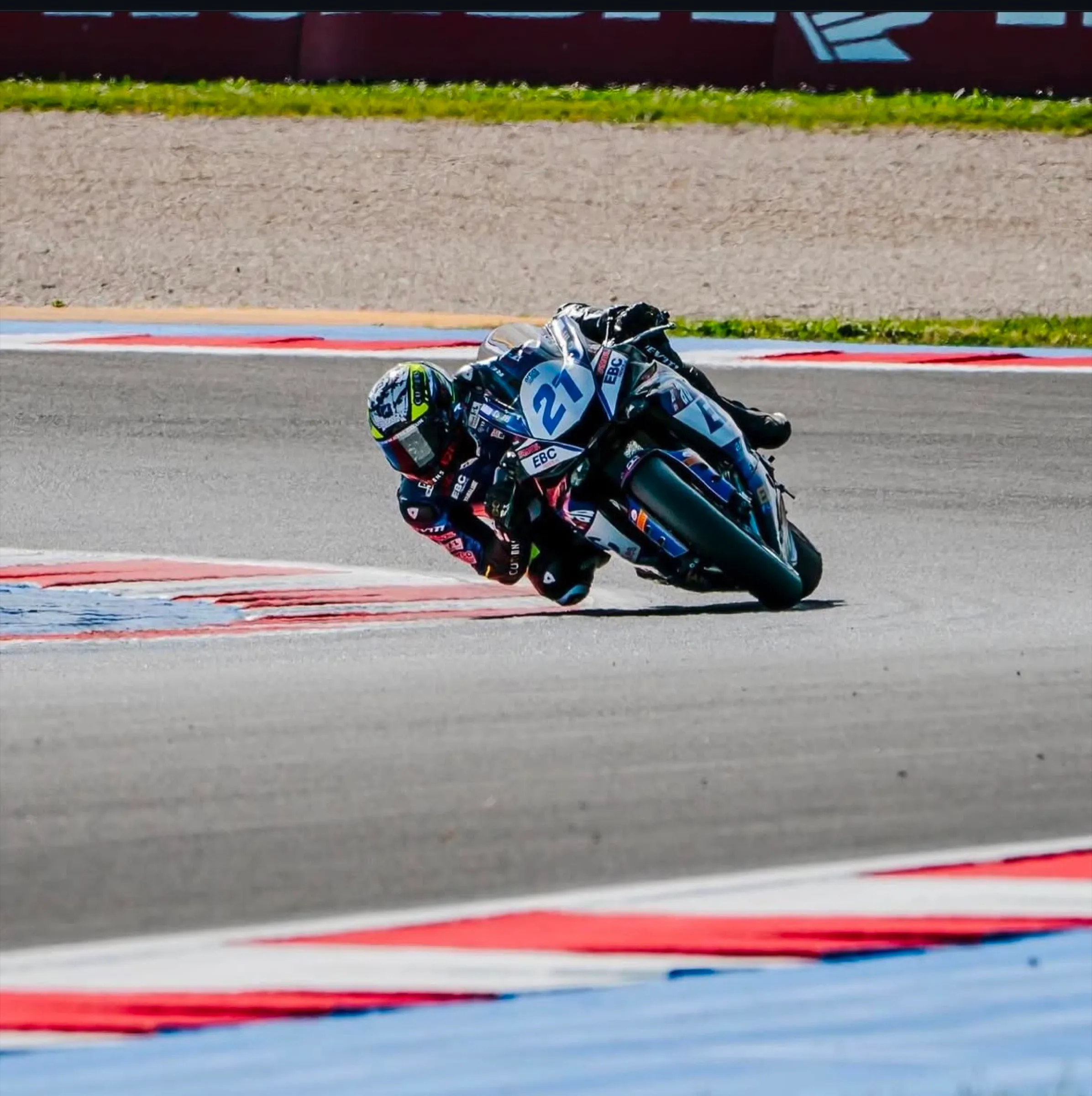 Superbike rider at full lean on a red and white kerb
